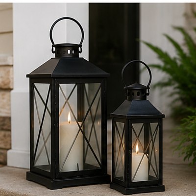 A pair of black lanterns with lit pillar candles glowing on a porch step